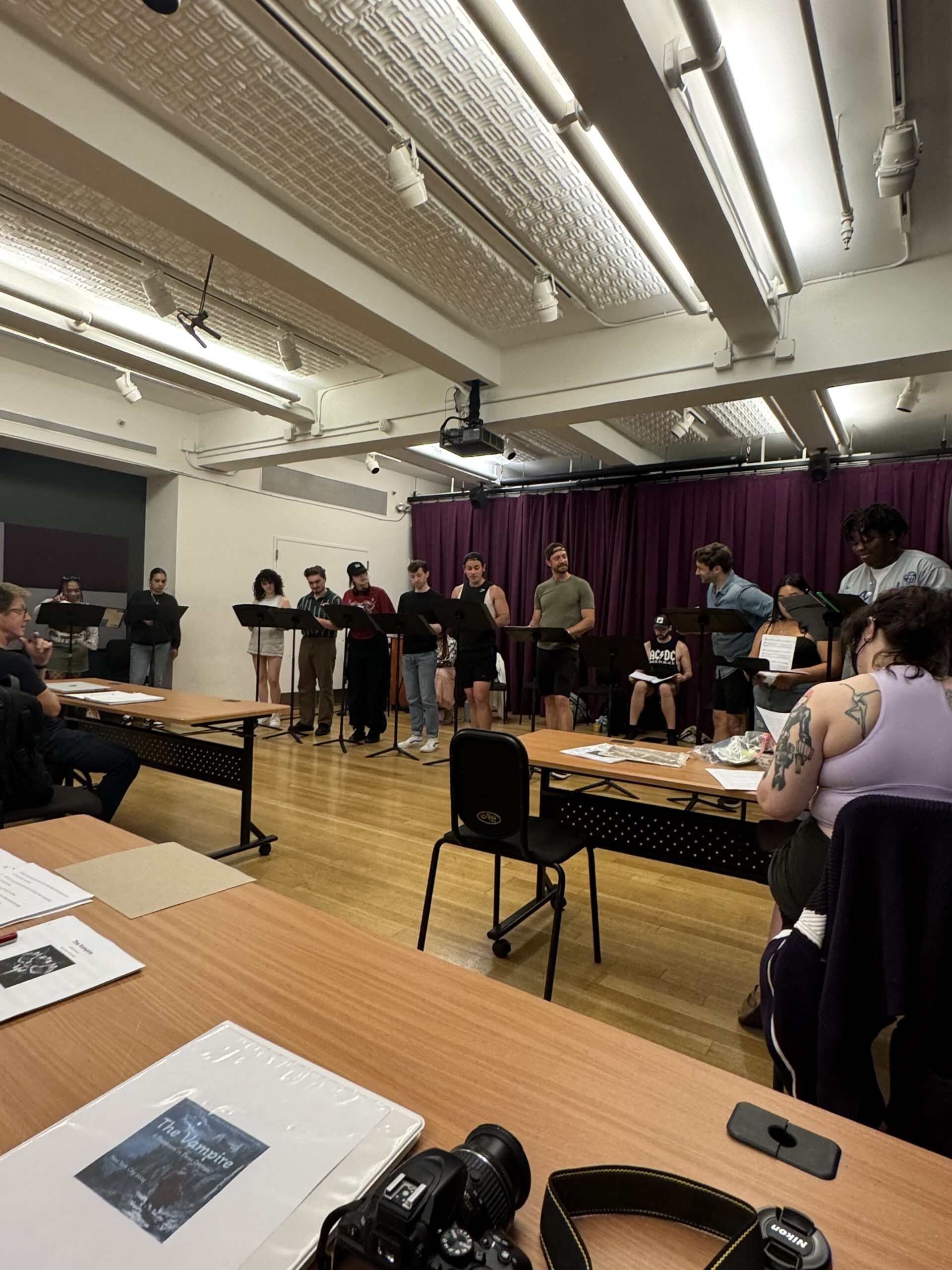A cast rehearses a performance on stage, with music stands and script sheets